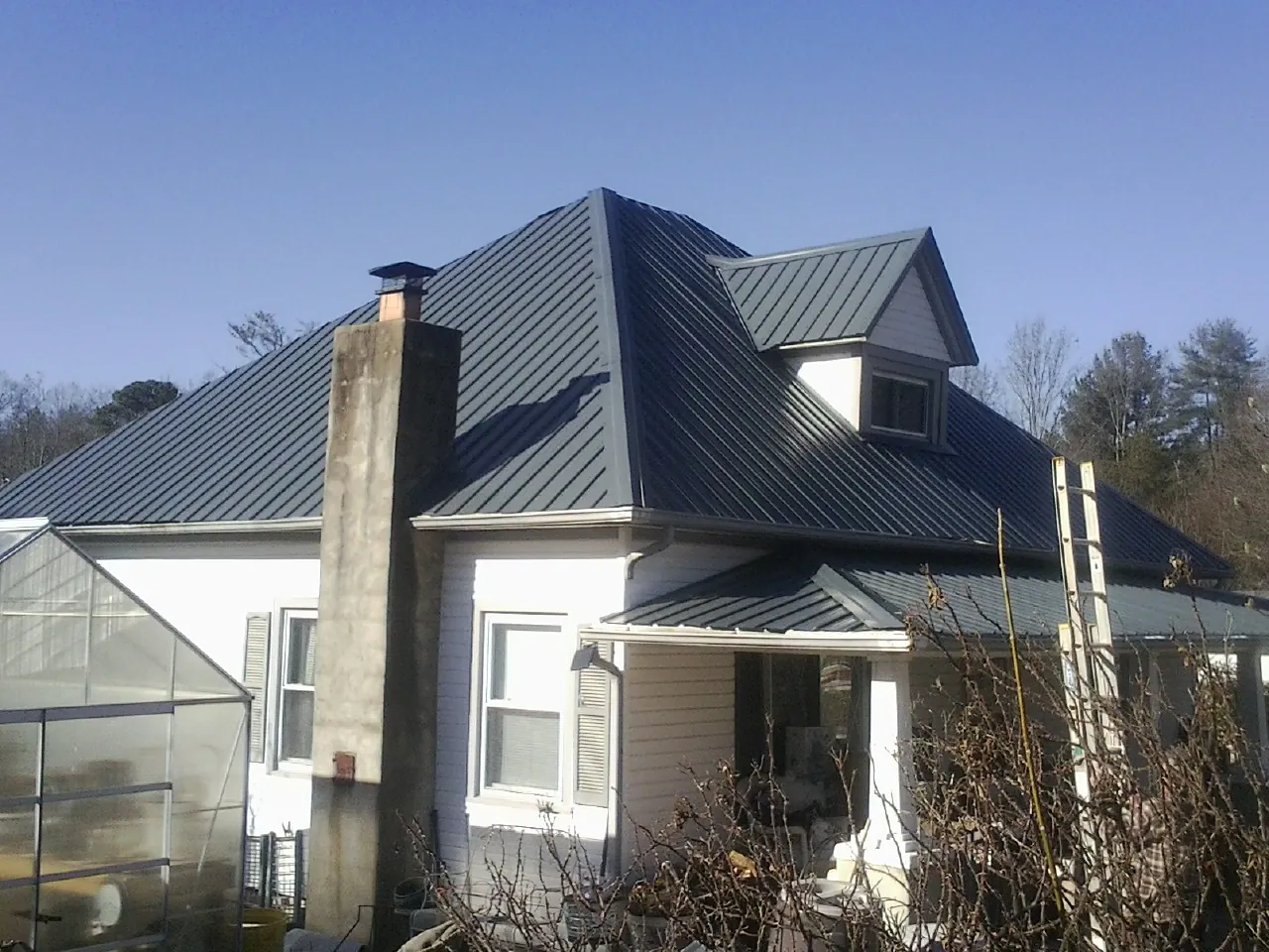 Dark blue standing seam metal roof on a white farmhouse with dormer — Slate & Tile Roof Repair by Roofing Brothers in Buena