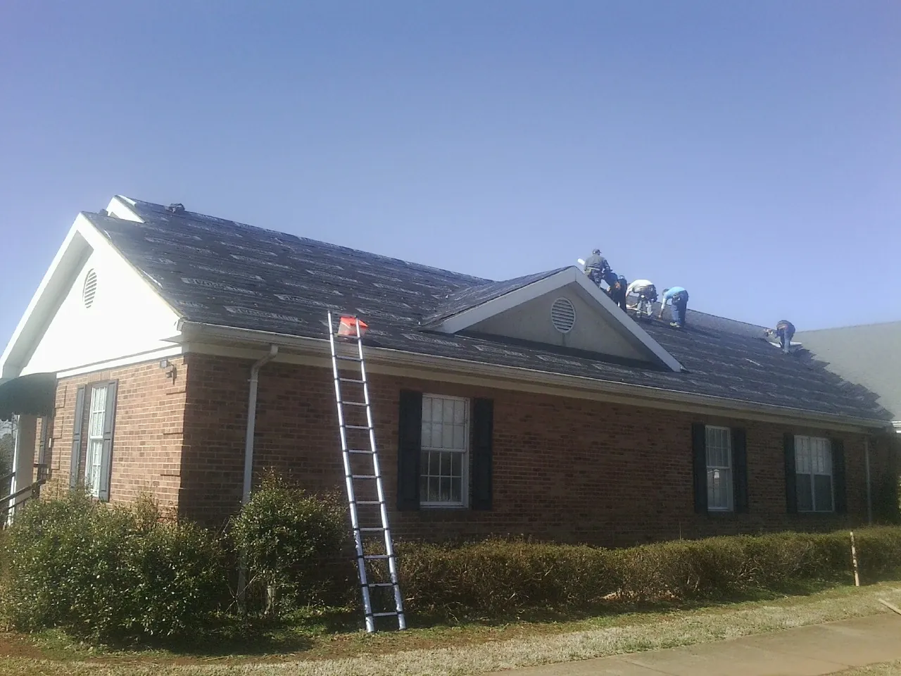 Crew tearing shingles off a brick ranch roof with a ladder set — Metal Roof Repair work by our crew in Buena