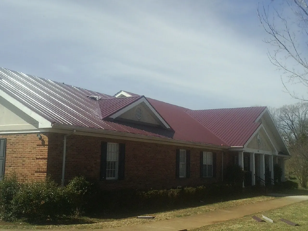 Red metal roof with gabled entries on a long brick building, from a Hail Damage Roof Repair job in Buena
